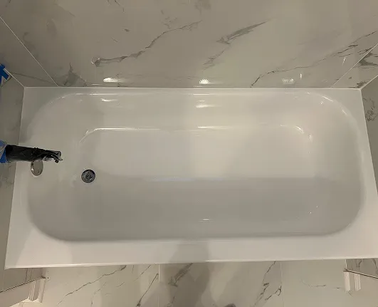 Professional bathtub refinishing with a smooth high-gloss white finish in a modern marble tile bathroom